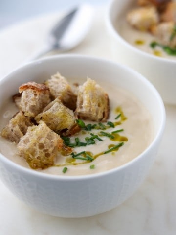 A close up of a bowl of cauliflower soup with croutons, chives and olive oil