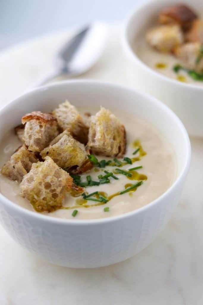 A close up of a bowl of cauliflower soup with croutons, chives and olive oil