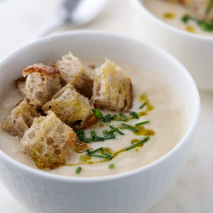 A close up of a bowl of cauliflower soup with croutons, chives and olive oil