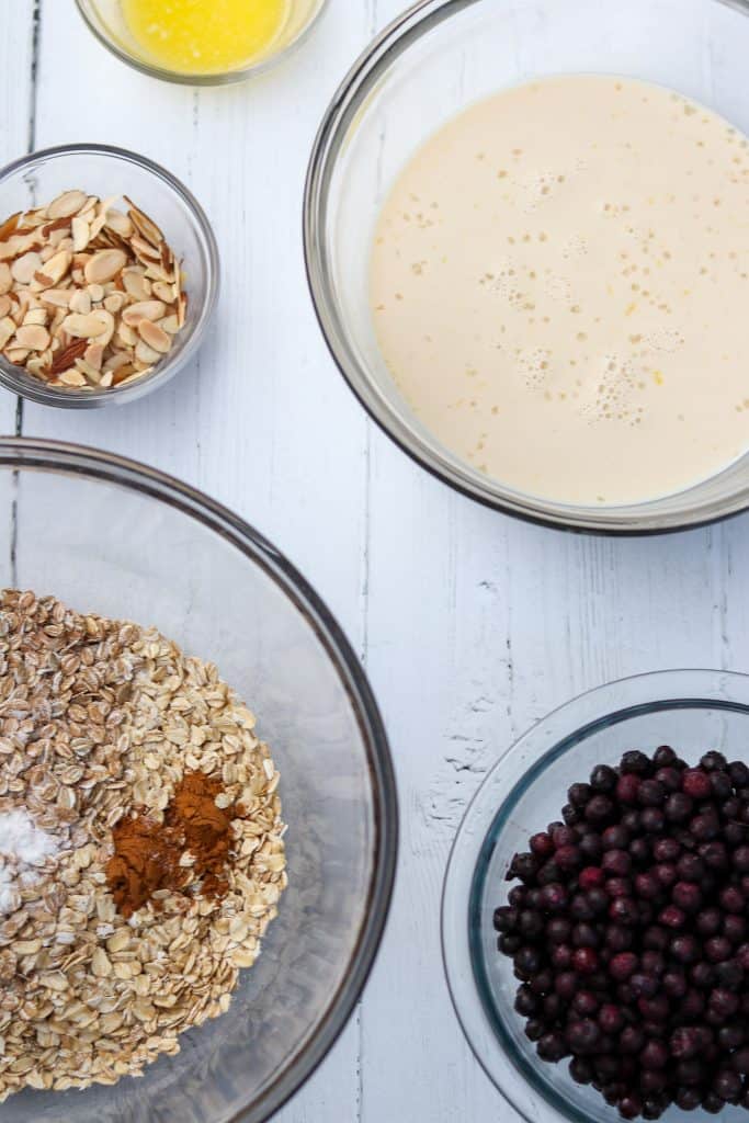 Bowls of milk, almonds, oats and blueberries on a wood surface