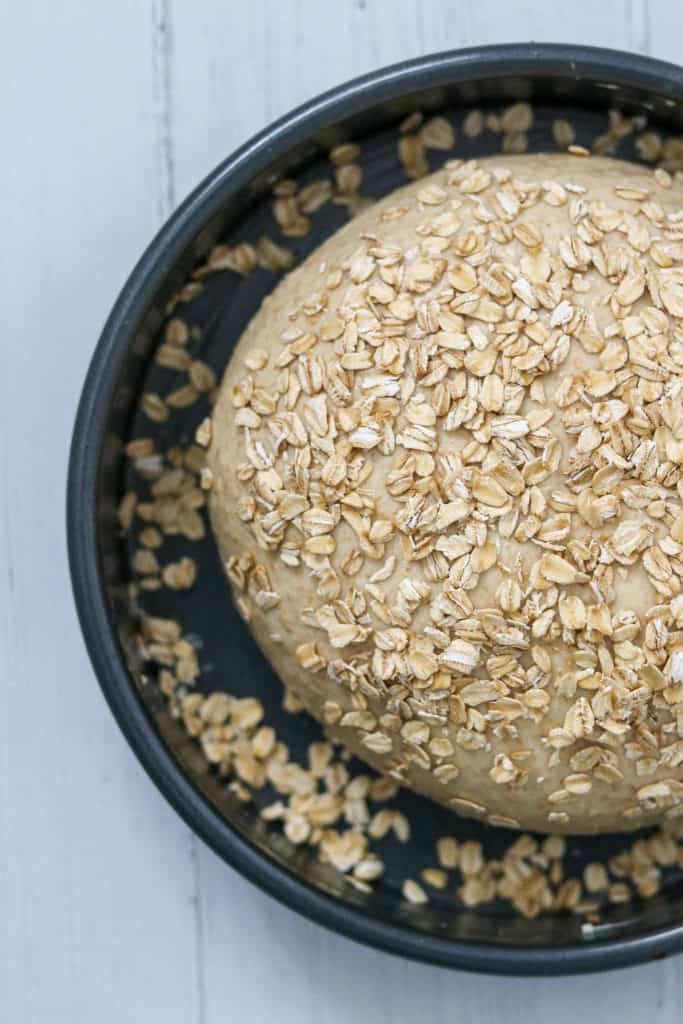 An unbaked loaf of oat bread covered in oats in a pan