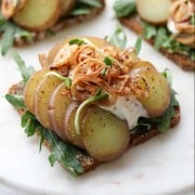 An open sandwich with lettuce, potato slices, crispy shallots and creamy sauce on a plate