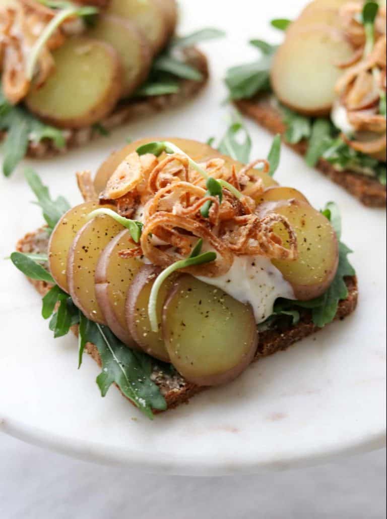 An open sandwich with lettuce, potato slices, crispy shallots and creamy sauce on a plate