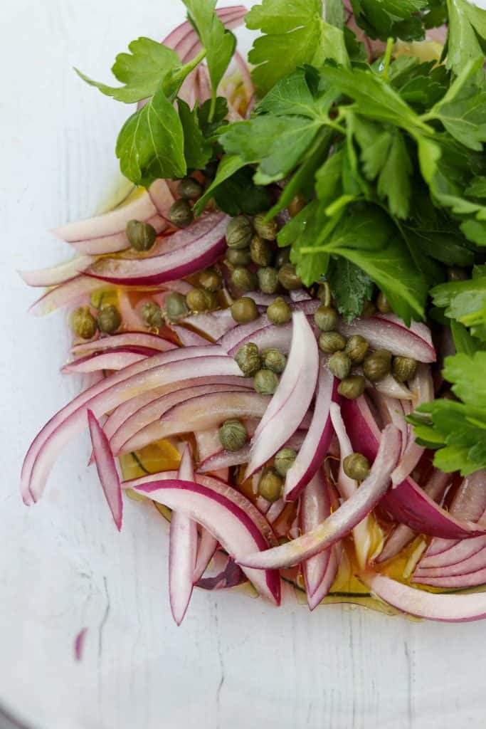 A close up of onions, capers, parsley and olive oil