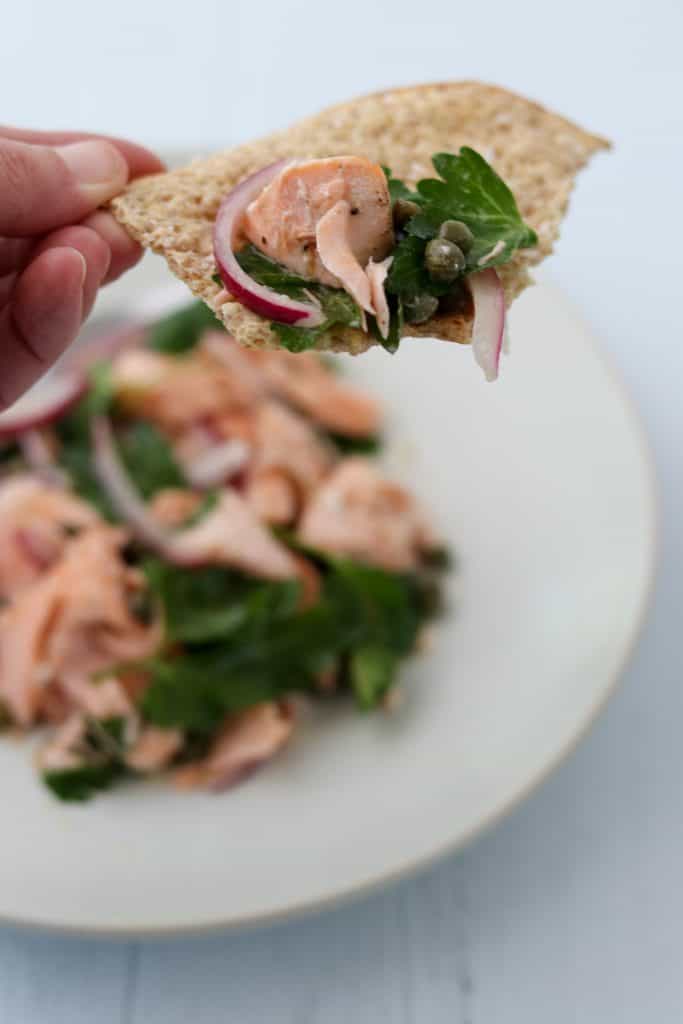 A close up of someone holding a piece of crispbread with salmon salad on top