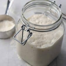 Sourdough starter in a jar next to a measuring cup with flour
