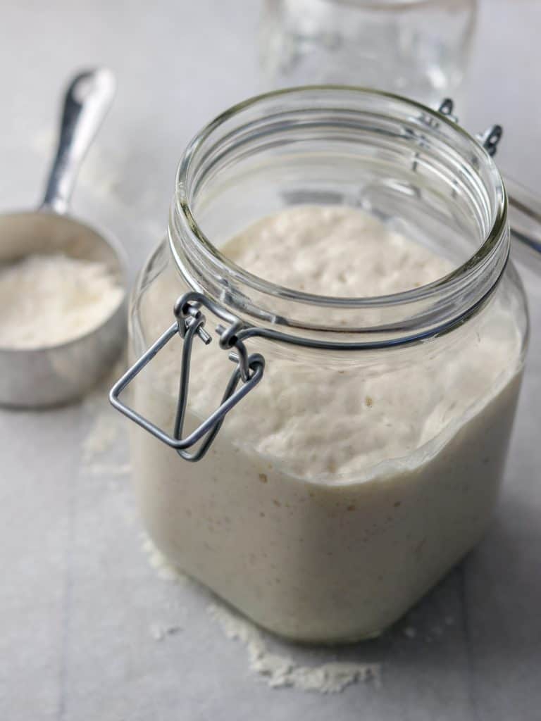 Sourdough starter in a jar next to a measuring cup with flour