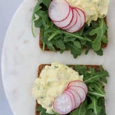 Two open face egg salad sandwiches topped with lettuce and radishes on a plate