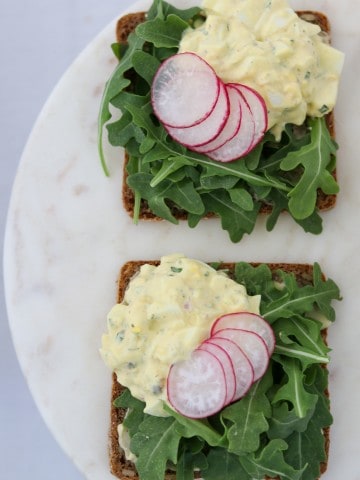 Two open face egg salad sandwiches topped with lettuce and radishes on a plate