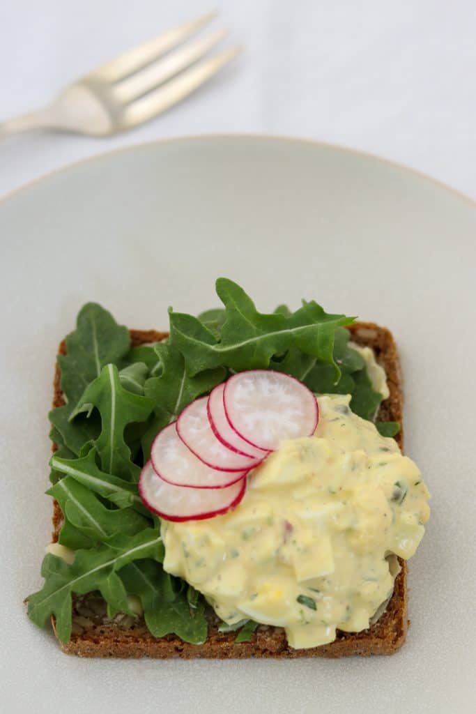 An open face egg salad sandwich topped with radishes and lettuce on a plate