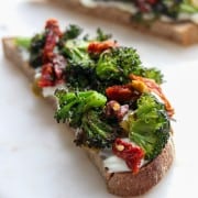 An open sandwich with ricotta cheese, broccoli and sun-dried tomatoes on a plate