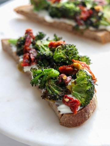 An open sandwich with ricotta cheese, broccoli and sun-dried tomatoes on a plate