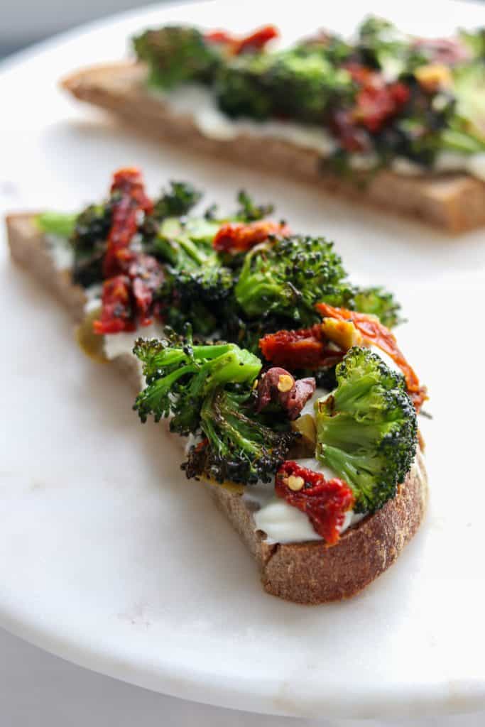 A close up of an open sandwich with ricotta, broccoli and sun-dried tomatoes