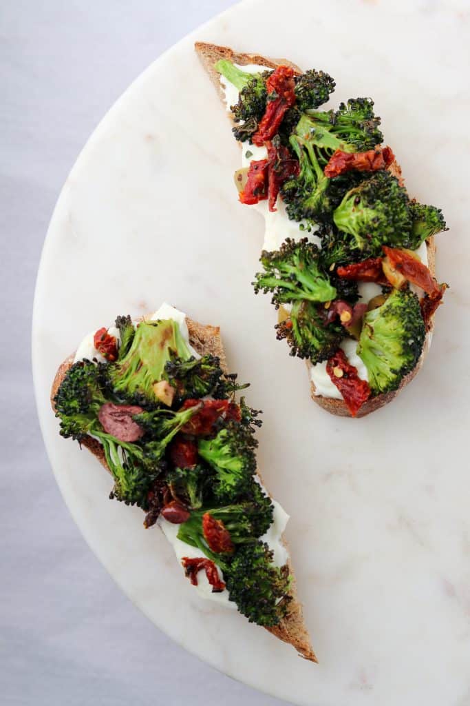 Two open sandwiches topped with ricotta cheese, broccoli and sun-dried tomatoes on a plate