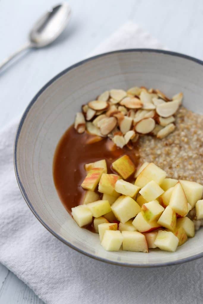 Oatmeal in a bowl with chopped apples, sliced almonds and caramel sauce