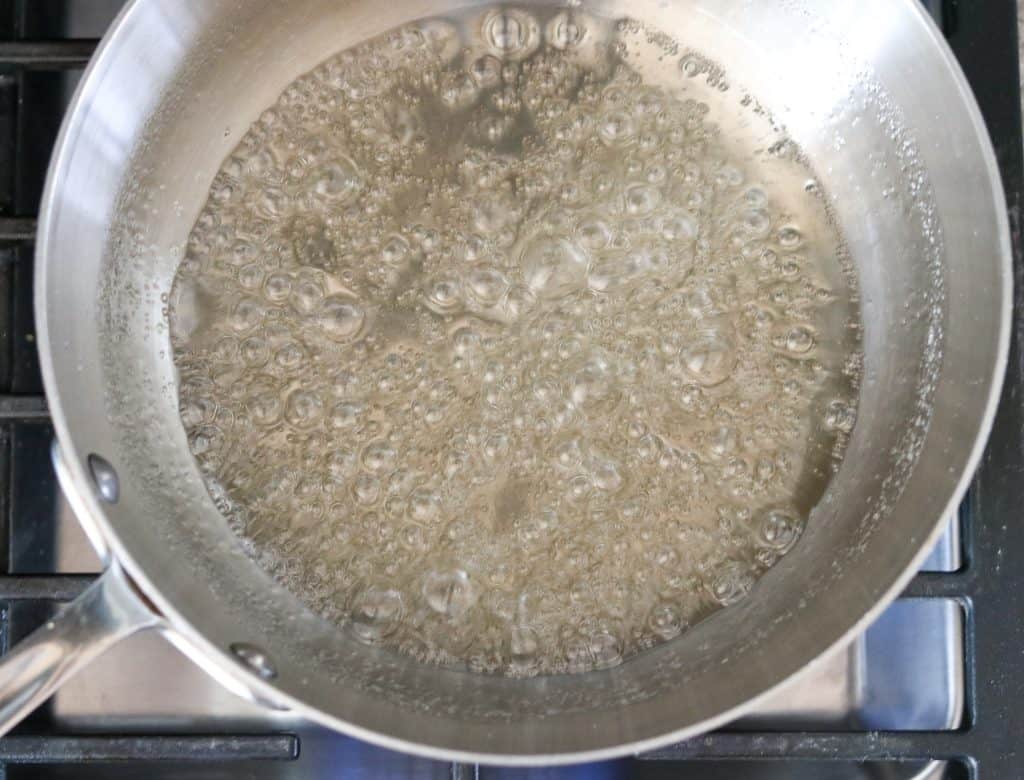 Sugar and water in a sauce pan boiling on a stove