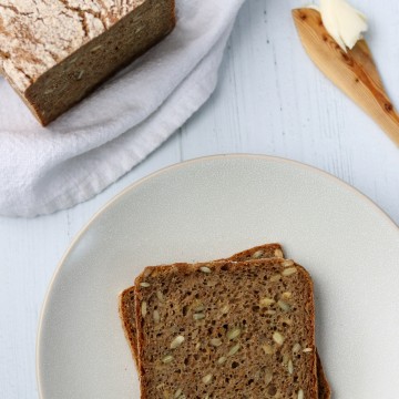 Rye bread slices on a plate next to a loaf of rye bread and a wooden knife with butter