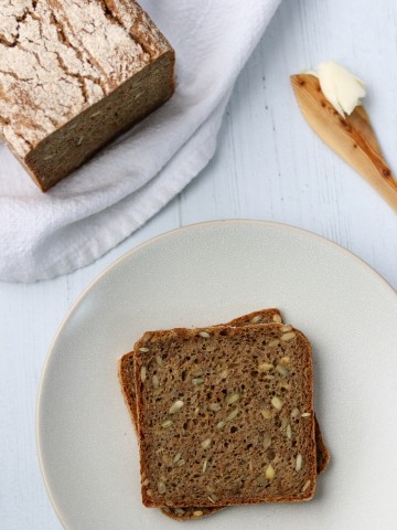 Rye bread slices on a plate next to a loaf of rye bread and a wooden knife with butter