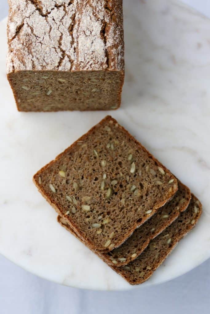 Three rye bread slices next to a loaf of rye bread on a plate
