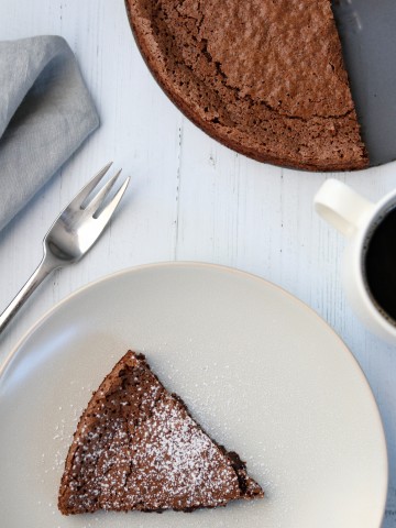 A piece of chocolate cake next to a fork, napkin and cup of coffee