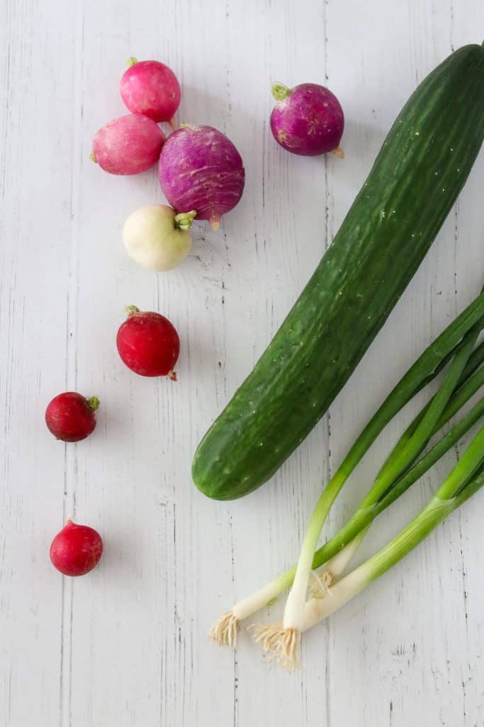 A cucumber, radishes and scallions on a wooden surface