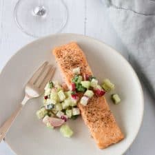 Salmon and cucumber radish relish on a plate with a fork, wine glass and napkin