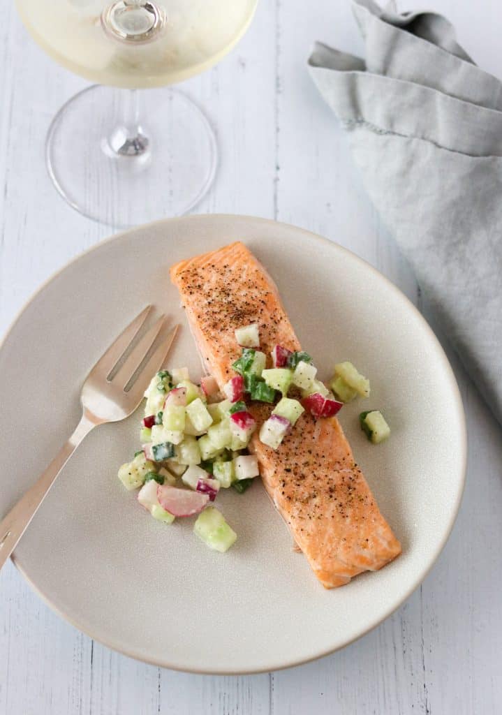 Salmon and cucumber radish relish on a plate with a fork, wine glass and napkin