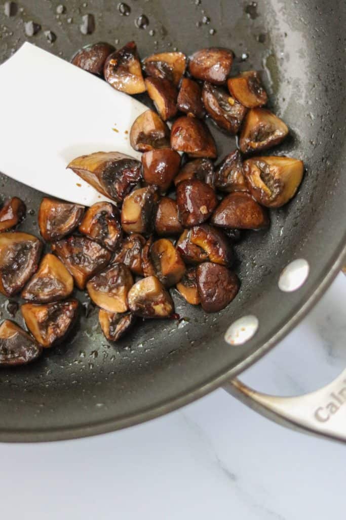 Mushrooms cooking in a pan with a spatula