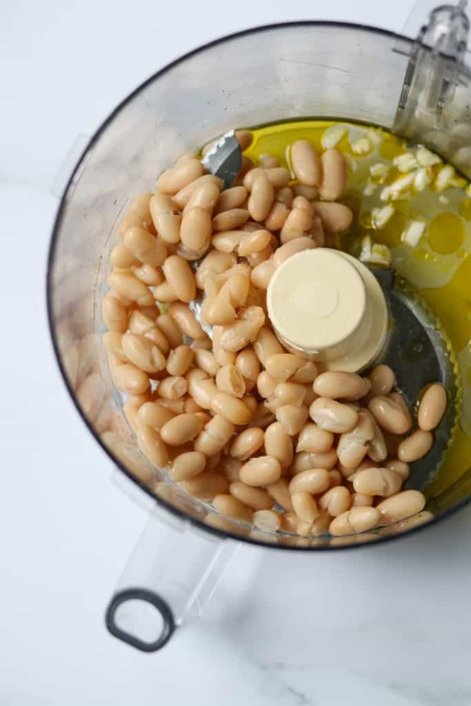 White beans, olive oil and garlic in the work bowl of a food processor