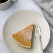 A slice of brown sugar skyr tart on a plate with a fork, napkin and a cup of coffee