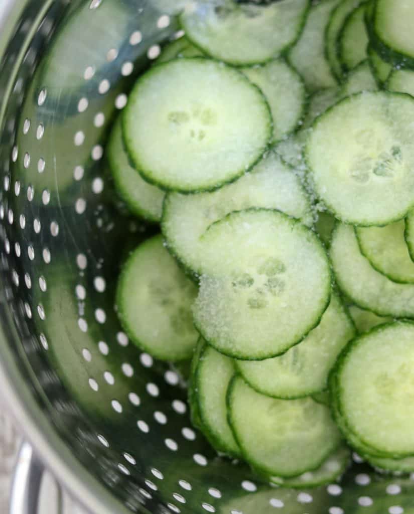 Cucumber slices in a colander sprinkled with salt