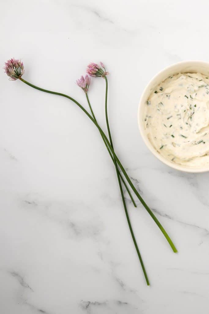 Creamy horseradish sauce in a bowl with fresh chive blossoms