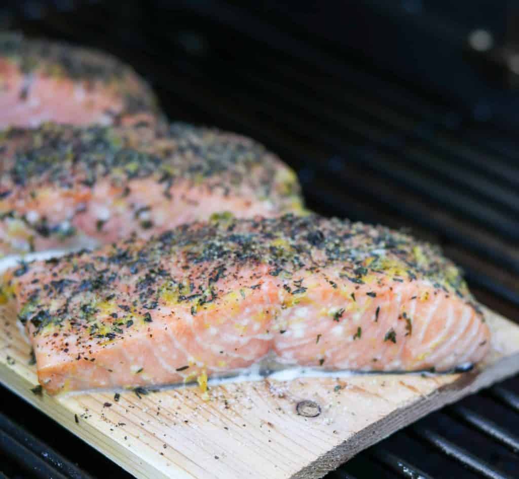 A close up of salmon filets on a cedar plank on the grill