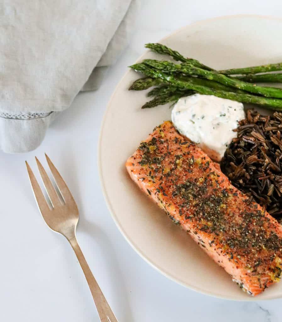 Grilled salmon, asparagus, wild rice and creamy sauce on a plate with a fork and napkin