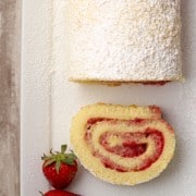 A slice of strawberry rolled cake on a plate with fresh strawberries