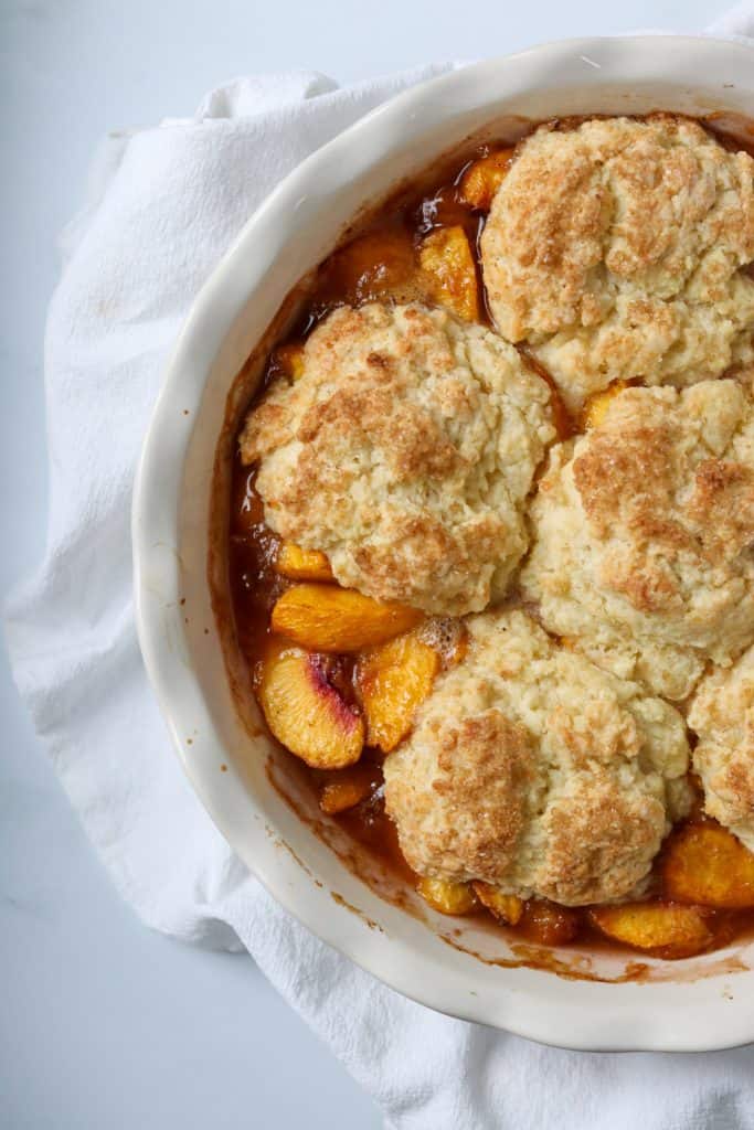 Peach cobbler in a white dish on a kitchen towel