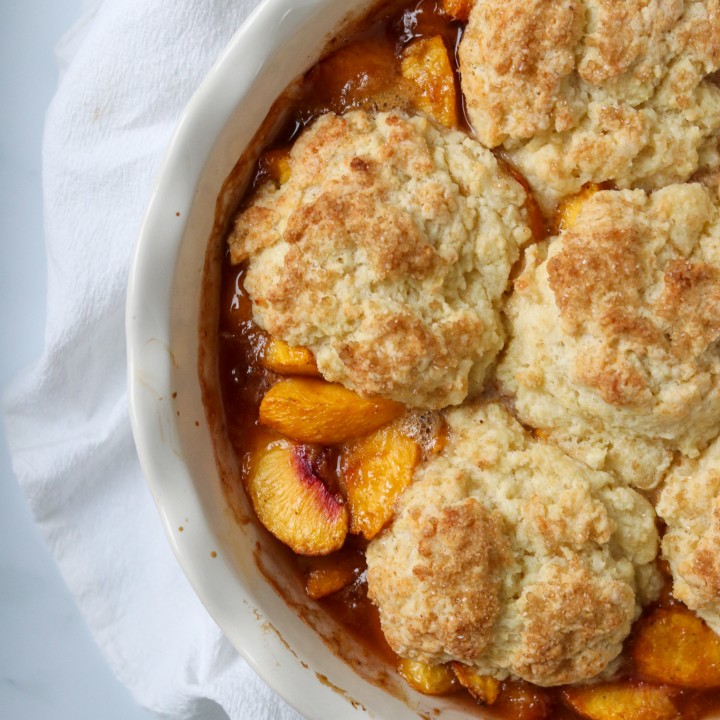 Peach cobbler in a white dish on a kitchen towel