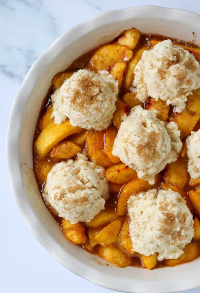 A dish filled with peach slices and topped with cobbler dough