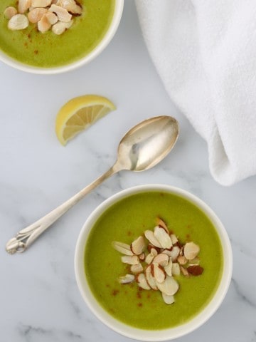 A bowl of zucchini soup topped with sliced almonds and a spoon and lemon wedge