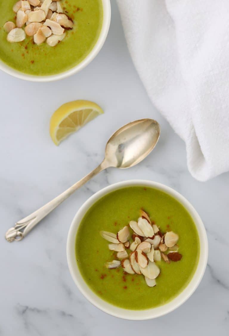 A bowl of zucchini soup topped with sliced almonds and a spoon and lemon wedge