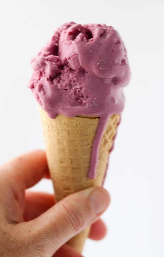 Person holding ice cream cone topped with frozen berry skyr yogurt