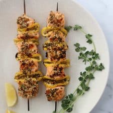 Salmon skewers on a plate with fresh herbs and lemon wedges