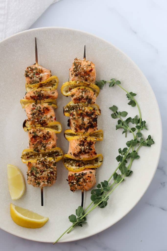 Salmon skewers on a plate with fresh herbs and lemon wedges