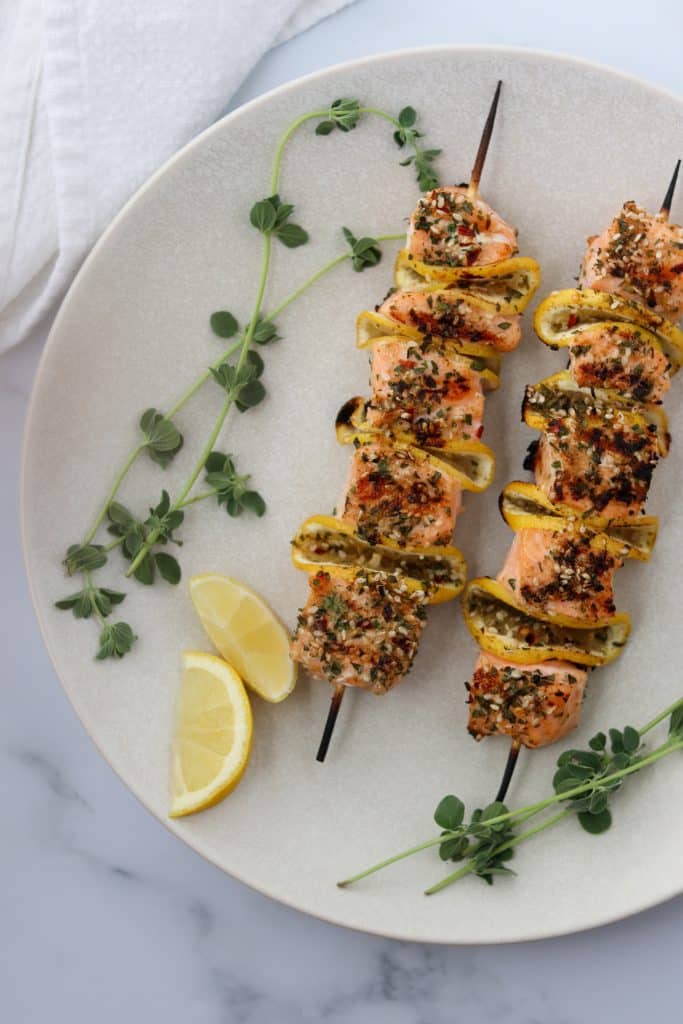 Salmon skewers on a plate with lemon wedges and fresh herbs