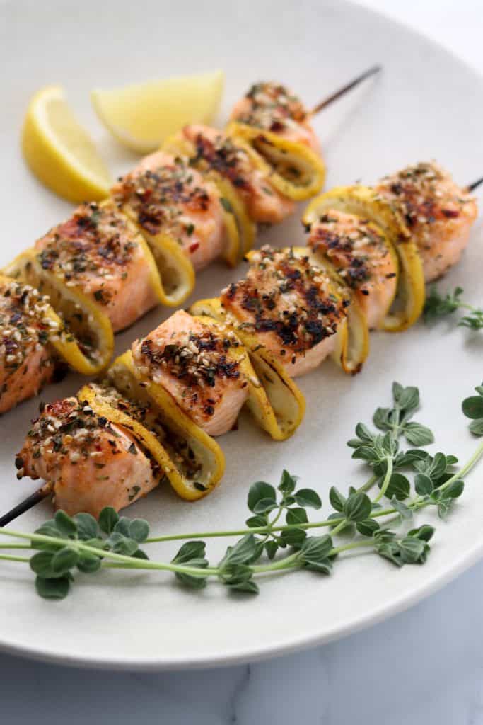 Salmon skewers on a plate with fresh herbs and lemon wedges