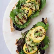 Open sandwiches topped with lettuce and grilled summer squash on a plate