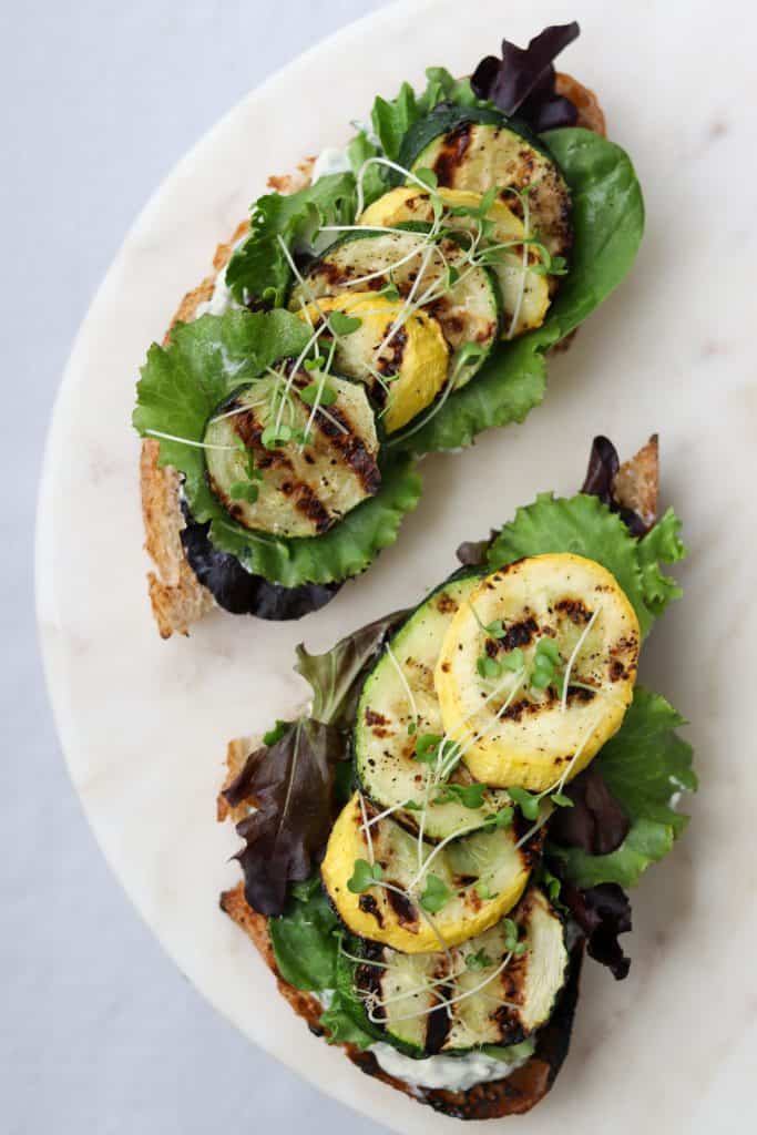 Open sandwiches topped with lettuce and grilled summer squash on a plate
