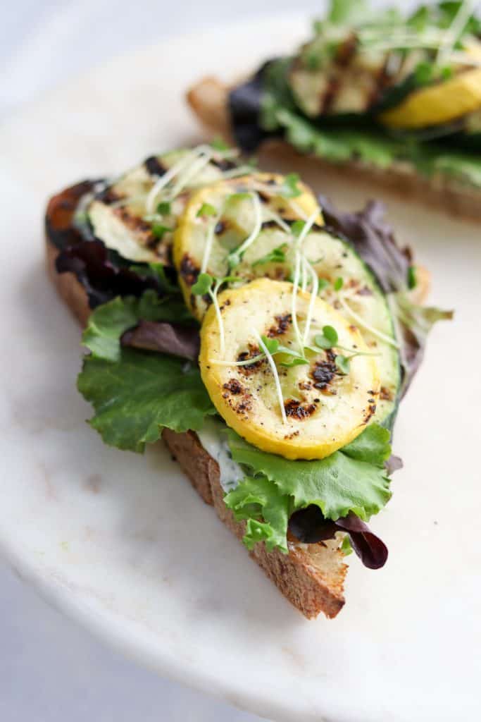 A close up of an open sandwich with grilled summer squash and lettuce