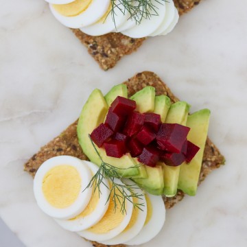 Toast with sliced egg, avocado and pickled beets on a plate