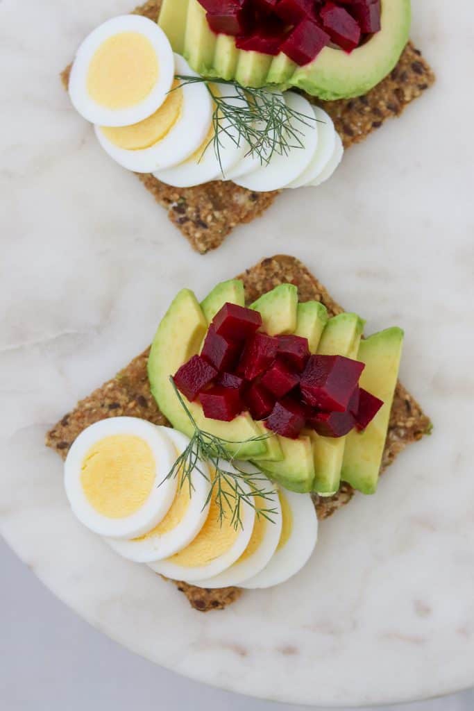 Toast topped with sliced egg, avocado and pickled beets on a plate